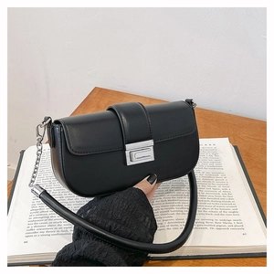Detail of black leather shoulder bag with silver clasp and chain strap on a vintage book
