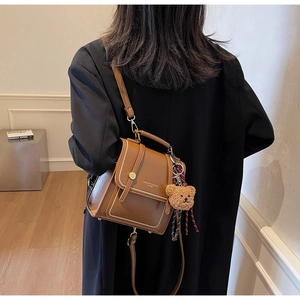 Detail of brown leather backpack featuring gold stud rivets and a cute bear charm
