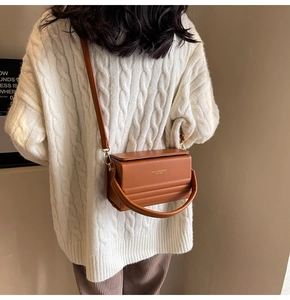 Close-up of caramel box bag with top handle and gold lettering on white sweater