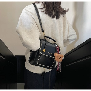 Detail of black leather handbag with gold clasp, brand text, and cute plush bear charm