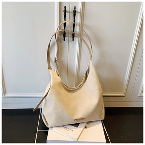 Detail of beige suede hobo bag featuring slim shoulder straps and a small metal logo plaque