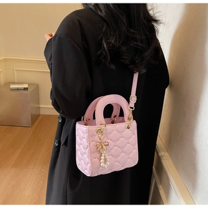 Détail d'un sac à main matelassé rose avec finitions dorées et nœud décoratif en perles