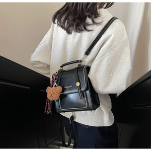Detail of glossy black leather backpack with gold logo, teddy charm and striped scarf accessory