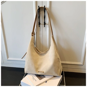 Detail of minimalist cream suede tote bag with brown leather strap and gold logo plate