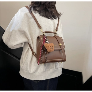 Rear view of brown vintage backpack with teddy bear charm on model against white wall