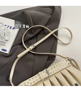 Close-up of beige pleated leather bag with silver studs and adjustable pin buckle strap