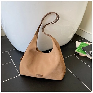 Close-up of matte camel hobo bag with gold buckle and brand plaque in a luxury setting
