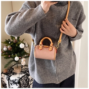 Détail du mini sac Boston rose avec lanières camel et garniture dorée sur pull gris