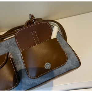 Detail of denim shoulder bag featuring leather pockets with white contrast stitching
