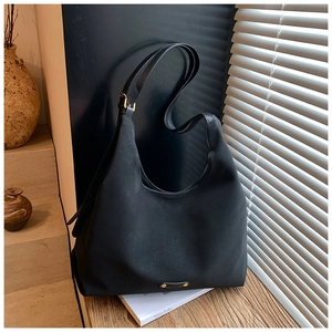 Close-up of matte black bucket bag showing golden metal plaque and refined texture