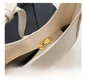 Macro shot of smooth gold zipper and dark wavy lining on creamy white shoulder bag