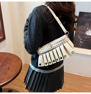 Detail of cream pleated shoulder bag with silver eyelets and rivet strap on model
