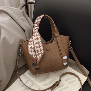 Brown lychee leather handbag with silk scarf detail and adjustable strap on a chair