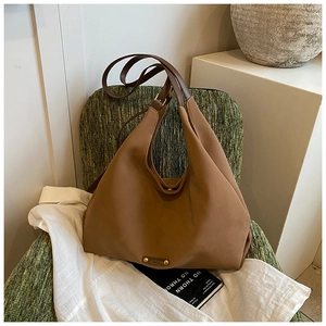 Detail of matte brown hobo bag with adjustable strap and golden rivets on dark green chair