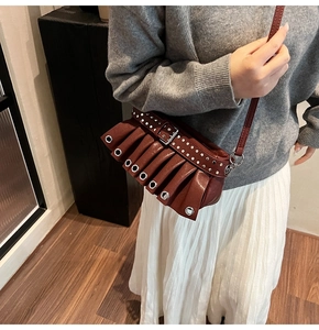 Close-up of pleated burgundy shoulder bag featuring silver metal rivets and eyelets detail