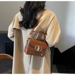 Brown leather crossbody bag with woven texture and gold clasp shown on a trench coat