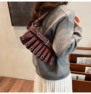 Close-up of deep red pleated shoulder bag with silver eyelets and rivet strap detail