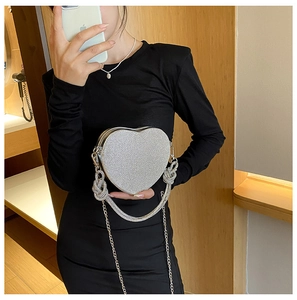 Détail d'un sac à main en forme de cœur orné de strass avec poignée tissée et chaîne en métal