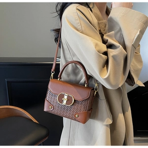 Detail view of brown vintage leather handbag with woven texture and gold clasp on trench coat