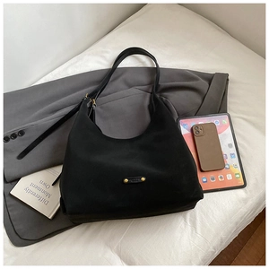 Detail of black matte hobo bag with gold logo plaque next to a tablet and blazer