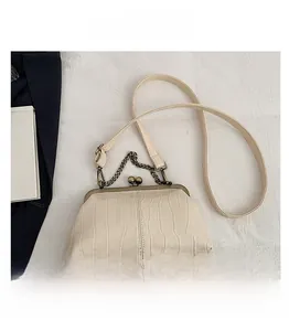 Detail view of cream crocodile texture bag with gold kiss-lock and phone size comparison