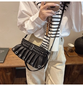 Close-up of black pleated leather shoulder bag with silver eyelets and studded belt detail