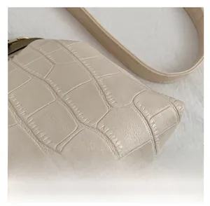 Detail of beige faux crocodile leather texture and bronze hardware on shoulder bag