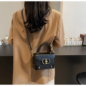 Detail of black box bag with golden buckle and woven texture on a fashion model