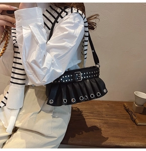 Detail of black pleated shoulder bag with punk metal eyelets and decorative buckle strap