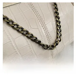 Detail shot of beige croc-embossed leather handbag with bronze chain and neat stitching