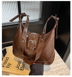Close-up of dark brown shiny patent leather crescent bag with silver buckles and grommets