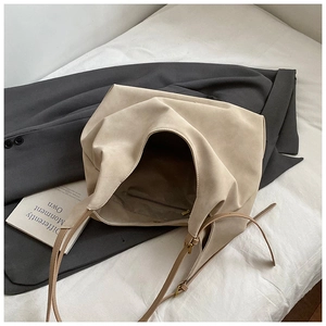 Minimalist beige oversized tote bag with matte texture and gold hardware on blazer background