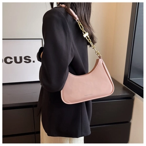 Detail of pink crescent underarm bag with thick gold chain worn by a female model
