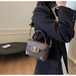 Close-up of brown woven leather handbag with gold twist lock on a model in black suit
