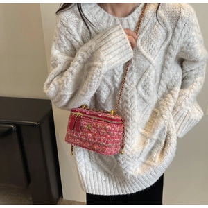 Close-up of pink tweed crossbody bag with gold flower buckle and chain strap on a model