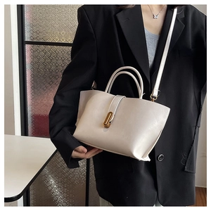 Close-up of beige tote bag showing gold oval twist lock and fine faux leather texture