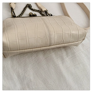 Detail of cream crocodile embossed small square bag with bronze metal clasp and chain