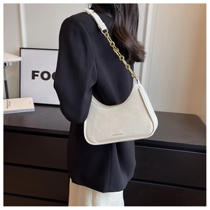 Detail of white underarm bag with gold chain strap and leather handle on a shoulder
