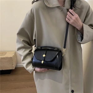 Classic black polished leather Boston bag with gold buckle worn on a khaki trench coat