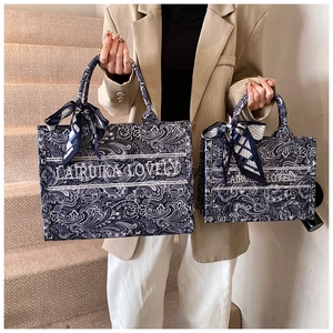 Dettaglio macro della borsa tote paisley blu con sciarpa di seta e striscia logo