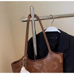 Detail of brown glossy tote bag with gold buckle and white pompom on metal hanger