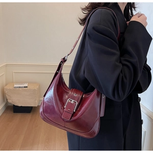 Close-up of burgundy patent leather shoulder bag with vintage metal buckle and glossy finish