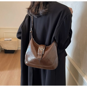 Detail of dark brown crescent shoulder bag with metallic buckle on black coat