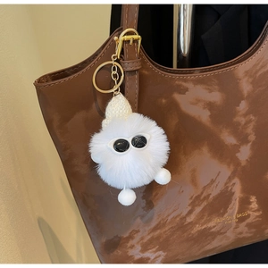 Detail of creative white fluffy monster charm with sunglasses on brown leather tote bag