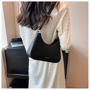 Modern black hobo bag with white text detail worn by a model in a minimalist office setting