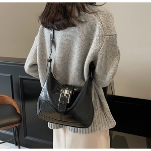 Detail of a black hobo bag with high-gloss leather and a large silver metal buckle strap