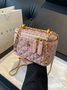 Pink tweed crossbody bag with gold camellia detail and chain strap held by hand
