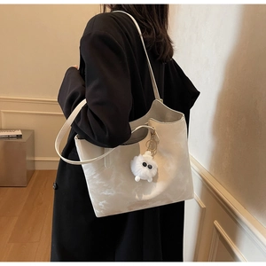 Close-up of a white marble texture tote bag with a cute plush charm on a black coat