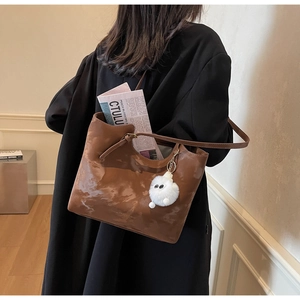 Brown large capacity tote bag with plush charm shown on female model in stylish coat