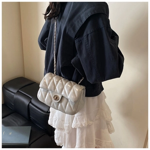 Détail d'un sac bandoulière matelassé gris montrant le cuir brillant et la chaîne argentée